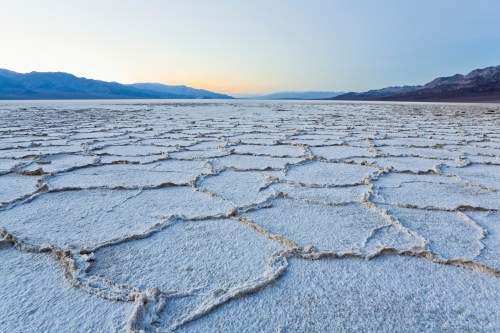 A vast salt flat with hexagonal patterns, surrounded by mountains under a soft sunrise sky.