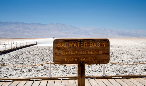 Sign for Badwater Basin, the lowest point in North America, with a vast salt flat and mountains in the background.