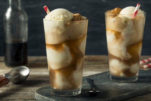 Two tall glasses of root beer floats with scoops of vanilla ice cream, served with striped straws on a wooden table.
