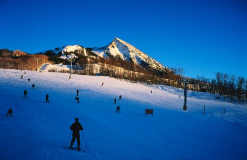 Skiers navigate a snowy slope with a mountain backdrop under a clear blue sky.