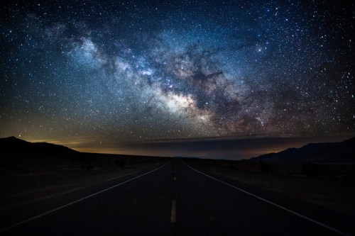 A starry night sky filled with the Milky Way over a deserted road stretching into the horizon.