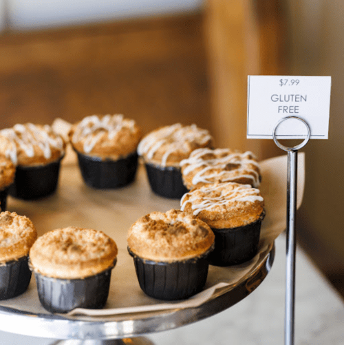 A display of gluten-free cupcakes on a stand, priced at $7.99, with a drizzle of icing on top.