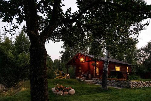 A cozy wooden cabin surrounded by trees, with a warm glow from the windows and a garden of flowers in the foreground.