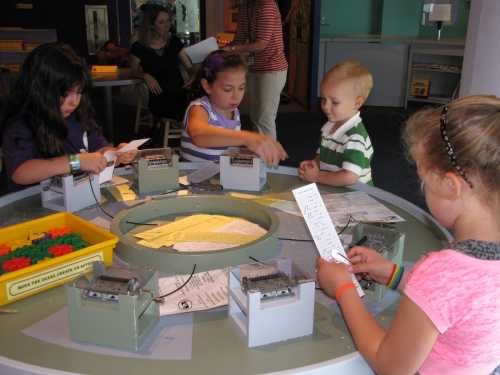 Children engaged in a hands-on activity at a table, working with papers and materials in a playful learning environment.