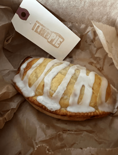 A golden pastry drizzled with icing, resting on crumpled paper, with a tag that says "I Like Pie."
