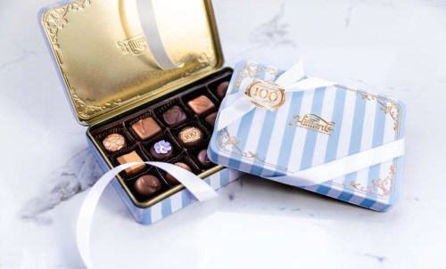 A decorative tin of assorted chocolates, partially open with a ribbon, showcasing a variety of sweet treats inside.