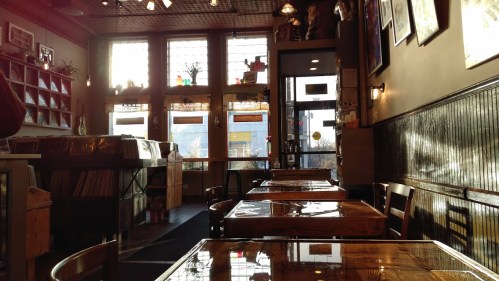 Cozy café interior with wooden tables, vinyl records, and sunlight streaming through large windows.
