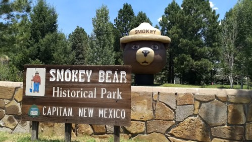 Sign for Smokey Bear Historical Park in Capitan, New Mexico, featuring a large Smokey Bear statue in the background.