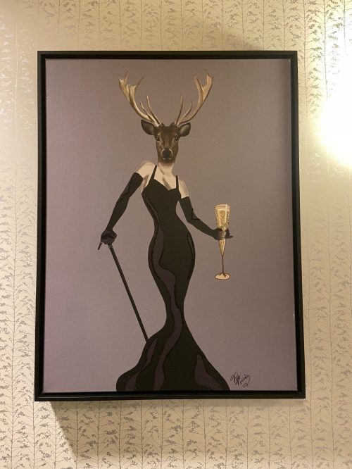 A stylish figure with a deer head in a black gown, holding a champagne glass and a cane, set against a patterned background.