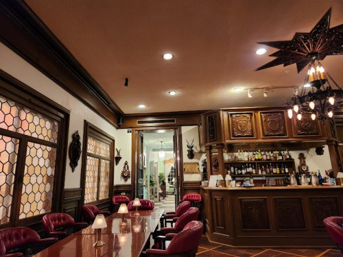 Elegant interior of a vintage-style bar with wooden decor, plush red seating, and a well-stocked bar in the background.