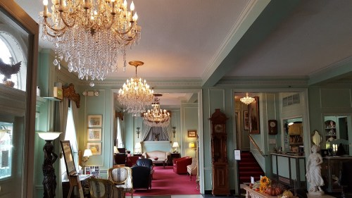 Elegant interior of a vintage lobby with chandeliers, plush seating, and decorative accents in soft green tones.
