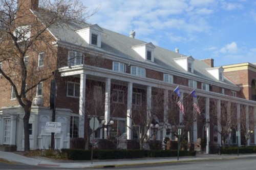 Historic brick building with white columns, flags, and trees, set against a blue sky.