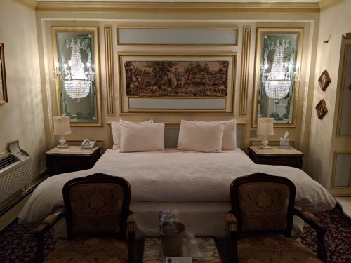 Luxurious hotel room featuring a king-sized bed, elegant decor, and ornate lighting fixtures.