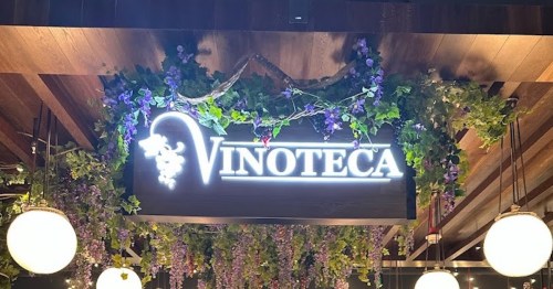 Sign for "Vinoteca" adorned with greenery and hanging lights, creating a cozy atmosphere.