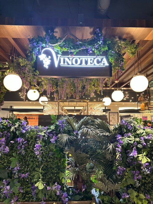 A cozy wine bar entrance adorned with greenery and purple flowers, featuring a sign that reads "Vinoteca."