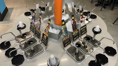 A circular condiment station with multiple dispensers and colorful signage for various sauces and toppings.