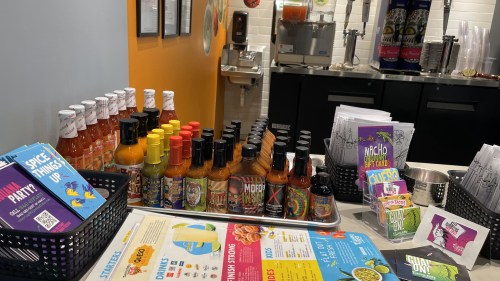A display of various hot sauces and condiments on a counter, with menus and promotional materials nearby.