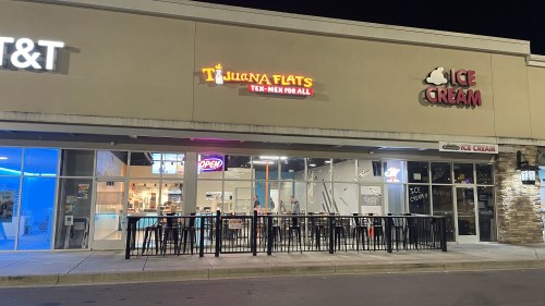 Exterior view of Tijuana Flats restaurant and ice cream shop at night, featuring bright signage and outdoor seating.