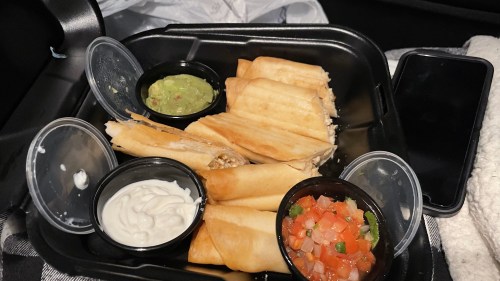 A takeout container with several rolled tacos, accompanied by guacamole, sour cream, and pico de gallo.