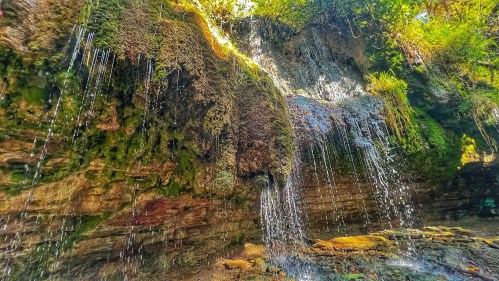 A serene waterfall cascading over moss-covered rocks, surrounded by lush greenery and sunlight filtering through the trees.