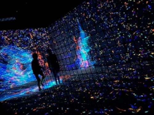 Silhouettes of two people walking through a vibrant, colorful light display on a wall.