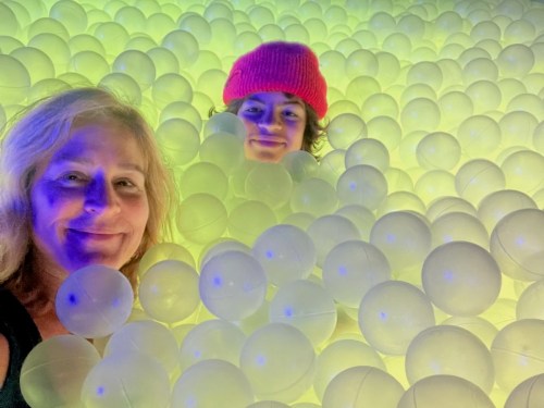 A woman and a child smile together in a colorful ball pit filled with translucent balls.
