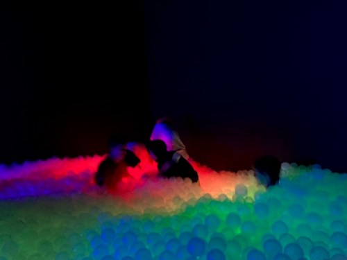 A colorful ball pit with glowing balls in various hues, featuring silhouettes of people playing and interacting.