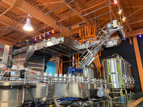 A modern beverage production line with shiny machinery and large tanks in a brightly lit facility.