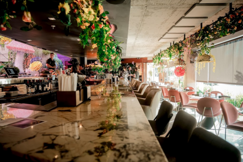 A stylish restaurant interior with a marble bar, colorful decor, and greenery hanging from the ceiling.