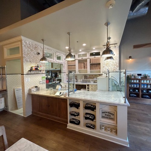 A cozy café interior featuring a wooden counter, pendant lights, and decorative wall patterns.
