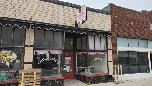 A charming storefront featuring a sign for chocolates and coffee, with large windows and a decorative awning.