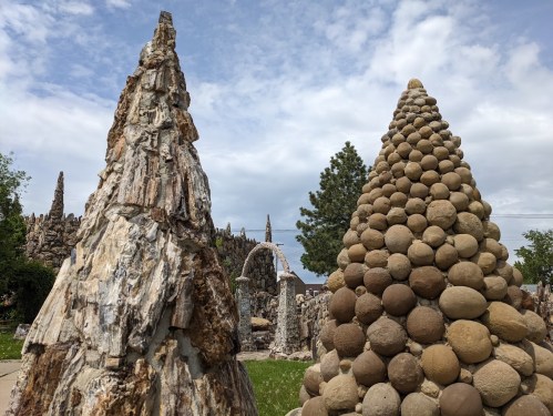 Two unique stone sculptures rise against a cloudy sky, one resembling a jagged peak and the other a smooth, rounded cone.