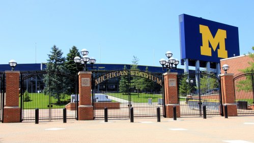 Entrance to Michigan Stadium, featuring a large "M" sign and landscaped grounds under a clear blue sky.