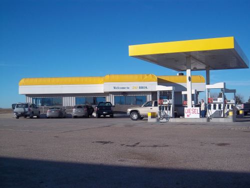 A gas station with a yellow roof, multiple cars parked, and a sign indicating diesel fuel availability.