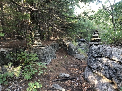 Two stone cairns stand on rocky terrain surrounded by trees in a forested area.