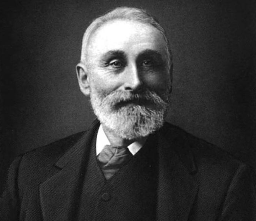 Black and white portrait of an older man with a beard, wearing a suit and tie, smiling at the camera.