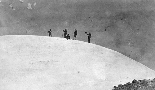A group of people standing on a snowy mountain peak, with a cloudy sky in the background.