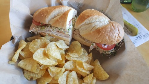 A sandwich with turkey, sprouts, and tomato, served with a side of crispy potato chips in a basket.