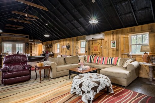 Cozy cabin interior with a sectional sofa, wooden walls, and a patterned rug, featuring warm lighting and rustic decor.
