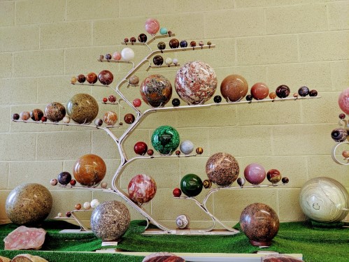 A decorative display of colorful spherical stones arranged on a tree-like metal stand against a green backdrop.