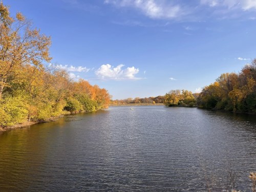 A serene river scene surrounded by autumn foliage under a clear blue sky.