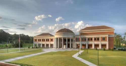 A modern building with a dome, surrounded by green lawns and trees, under a cloudy sky.