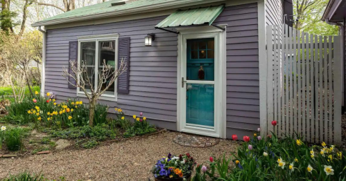 A charming purple house with a green roof, surrounded by colorful flowers and a white picket fence.