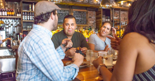 A group of friends enjoying food and drinks at a lively bar, engaged in conversation and laughter.