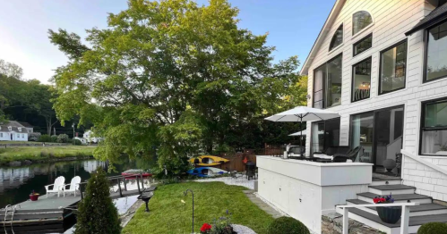 A serene lakeside home with a patio, lush greenery, and kayaks by the water, reflecting a peaceful outdoor setting.
