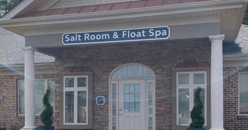 Exterior of a spa building with a sign that reads "Salt Room & Float Spa," featuring stone accents and large windows.