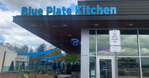 Exterior of Blue Plate Kitchen with a sign, outdoor seating, and a 15-minute parking sign.
