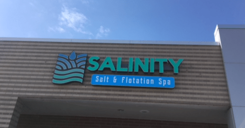Sign for "SALINITY Salt & Flotation Spa" on a brick building under a clear blue sky.