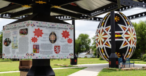 A large, colorful egg sculpture with informational signage nearby, set in a grassy area.