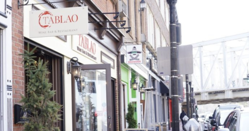 A street view featuring the sign for "Tablao Wine Bar & Restaurant" alongside other storefronts and a bridge in the background.